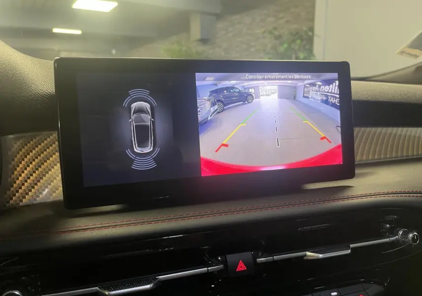 Écran central de l'Alfa Romeo Tonale rouge montrant la caméra de recul avec guidage et capteurs de proximité.