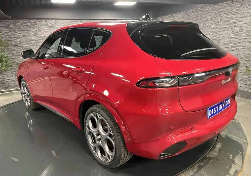 Vue 3/4 arrière droite d'un Alfa Romeo Tonale rouge avec jantes alliage 20 pouces et toit noir en intérieur showroom.