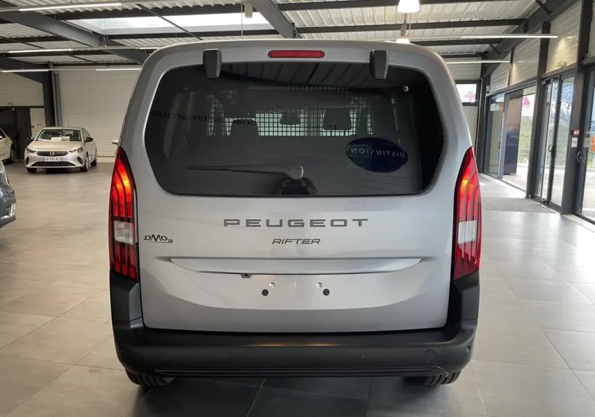 Vue arrière d'un Peugeot Rifter gris Artense avec feux verticaux LED et pare-chocs noir dans un showroom.