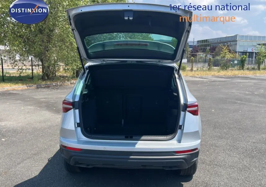 Vue arrière d'un Skoda Karoq 1.5 TSI 150CH DSG7 en Reflex Silver Metal avec coffre ouvert sur un parking extérieur.