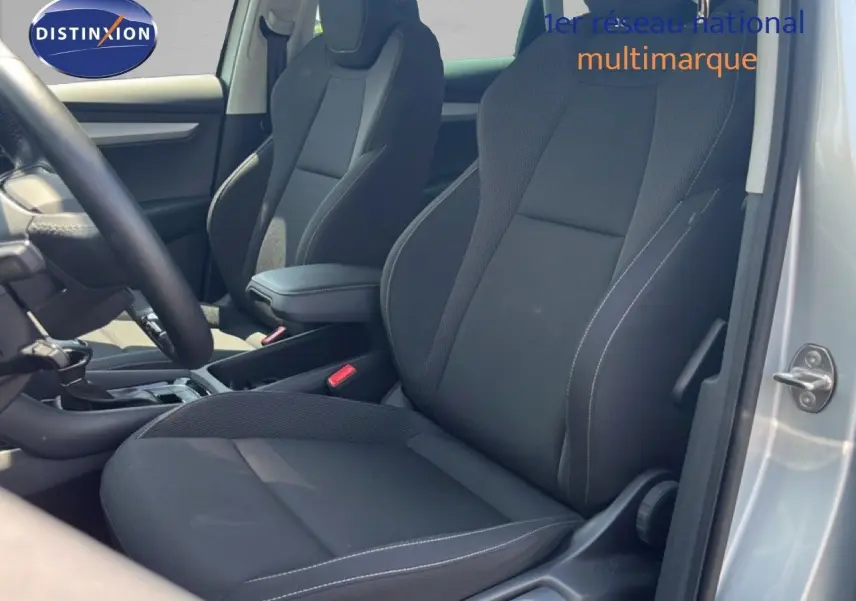 Vue intérieure côté conducteur du Skoda Karoq 1.5 TSI 150ch en tissu noir avec accoudoir central, porte ouverte couleur argent.