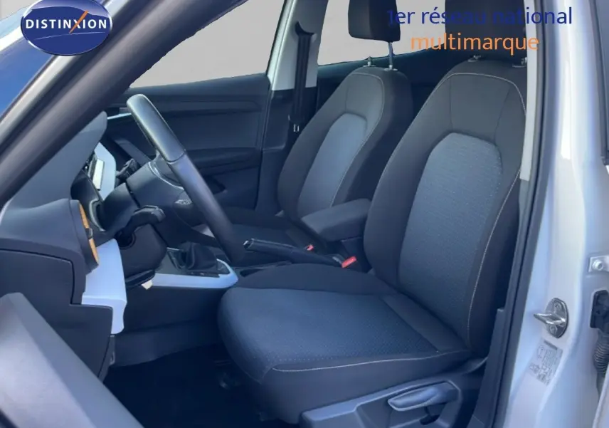 Vue intérieure côté conducteur d'une SEAT Arona blanche, mettant en valeur les sièges tissu gris et la console centrale.