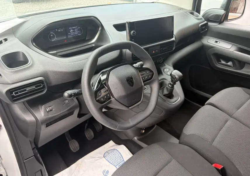 Vue intérieure côté conducteur du Peugeot Partner 2026, volant multifonctions, écran tactile et boîte manuelle visibles.