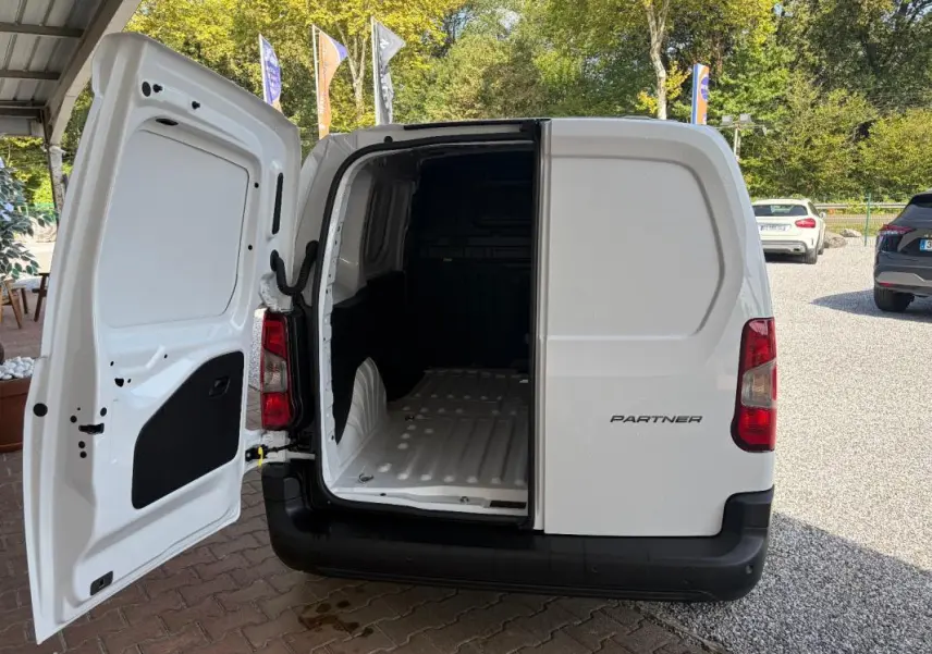 Vue arrière d’un Peugeot Partner blanc 2026 avec porte arrière gauche ouverte montrant l’espace de chargement vide.