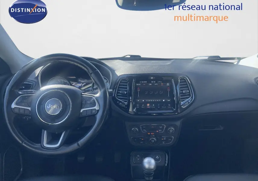 Vue intérieure du tableau de bord et volant du Jeep Compass gris foncé, avec écran tactile et levier de vitesse manuel visible.