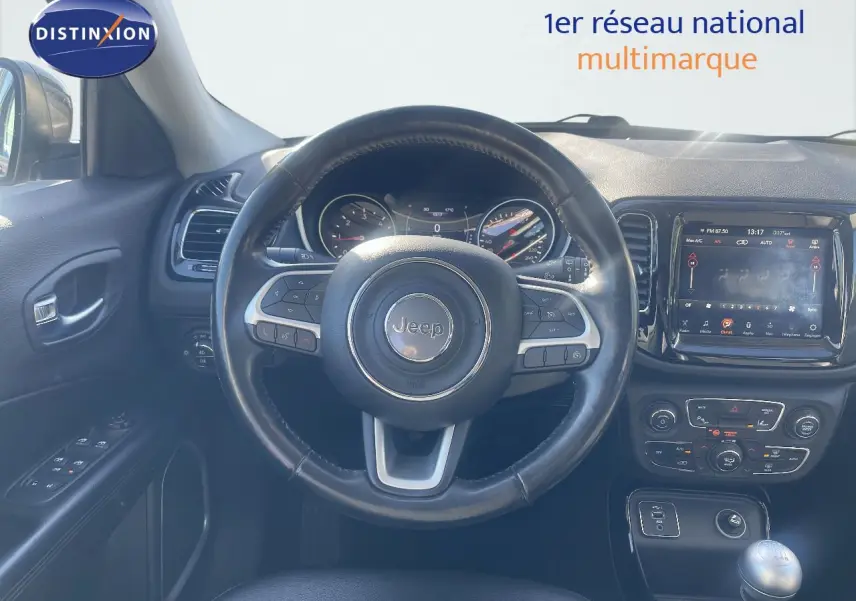 Vue intérieure centrée sur le volant Jeep Compass gris foncé, tableau de bord et console avec écran tactile visible.
