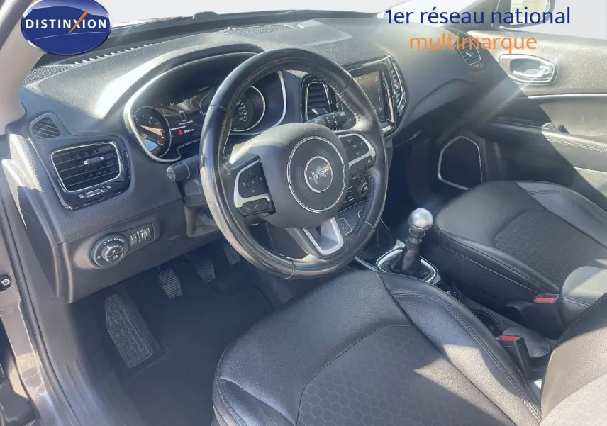 Vue intérieure côté conducteur du Jeep Compass gris foncé, mettant en valeur le volant multifonction et la boîte manuelle.