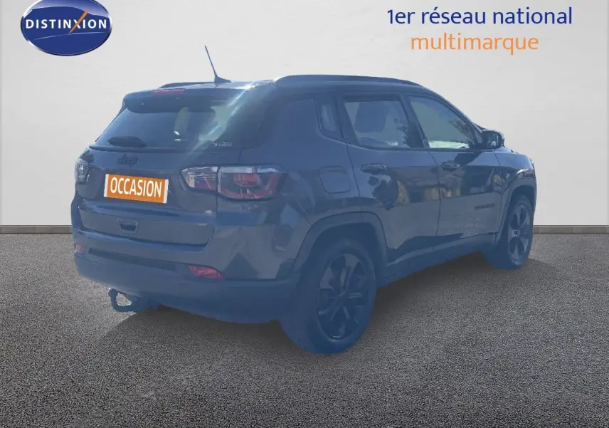 Jeep Compass gris foncé en 3/4 arrière droit, version Brooklyn Edition avec jantes noires et attelage visible.
