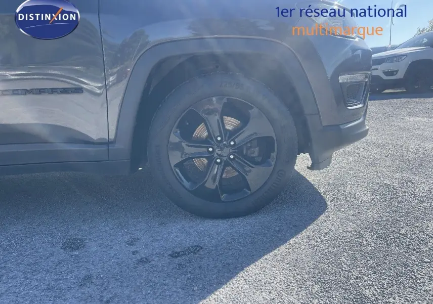 Vue latérale centrée sur la roue avant droite d'un Jeep Compass gris foncé avec jante noire brillante.