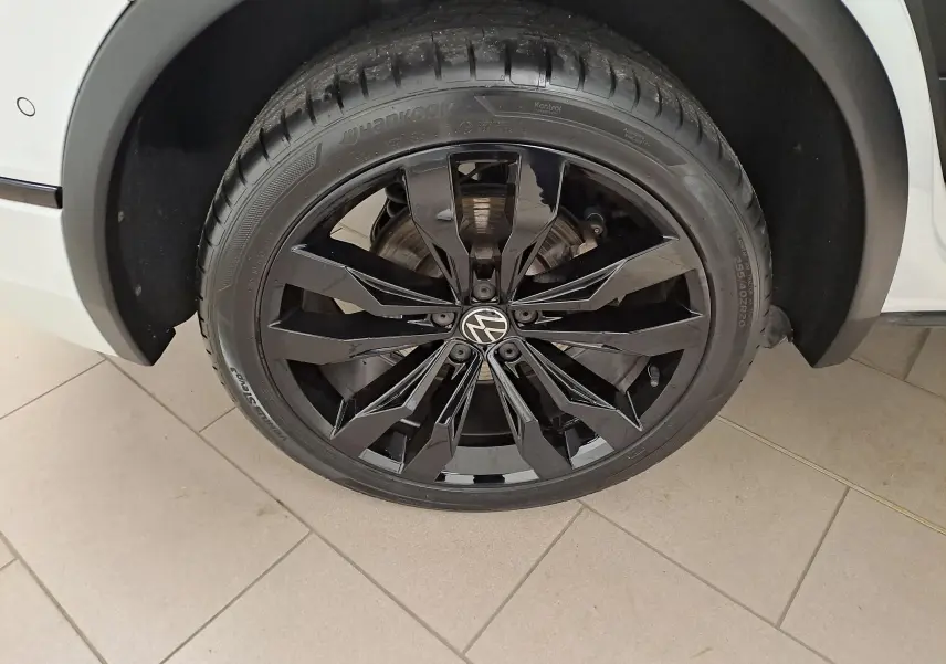Gros plan sur la roue avant droite du Volkswagen Tiguan blanc nacré avec jante alliage noir 20 pouces Suzuka.