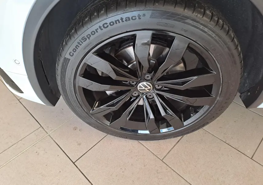 Gros plan sur la jante noire 20'' Suzuka du côté avant gauche d'un Volkswagen Tiguan blanc nacré 2023.