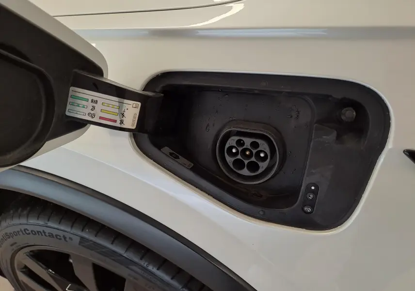 Prise de recharge hybride ouverte côté gauche sur Volkswagen Tiguan blanc nacré avec jante noire visible en bas.