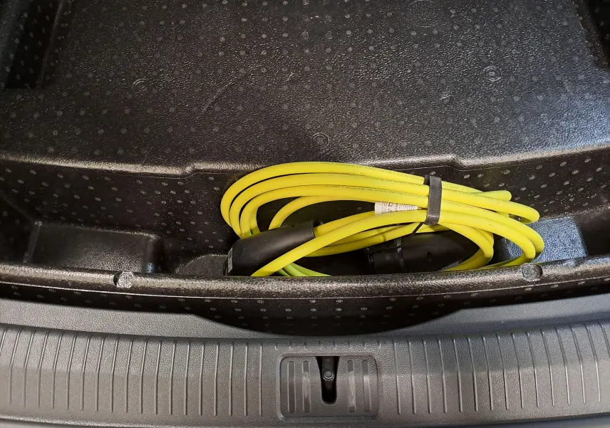 Câble de recharge jaune enroulé dans le coffre d’un Volkswagen Tiguan blanc nacré hybride rechargeable, vue intérieure arrière.