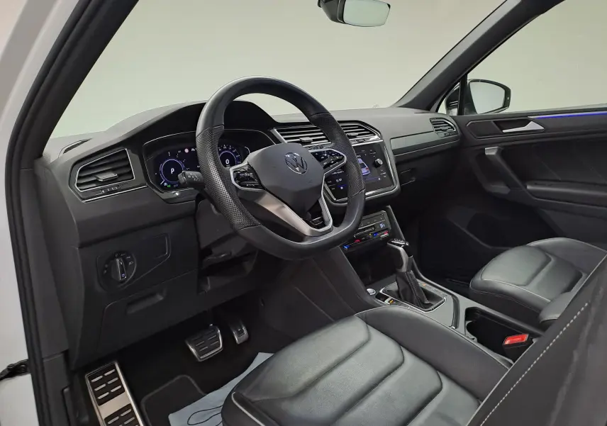 Vue intérieure côté conducteur du Volkswagen Tiguan 1.4 eHybrid 2023, volant cuir, tableau de bord numérique et sellerie noire.
