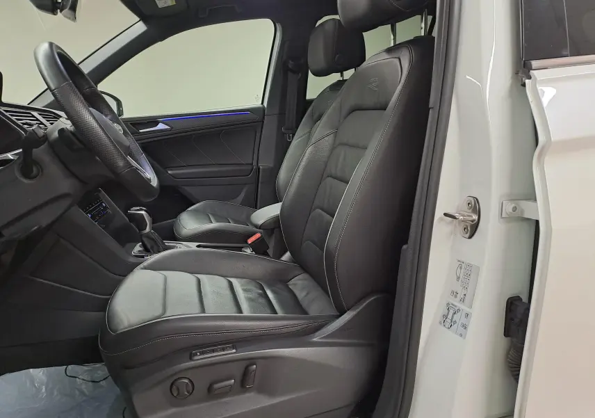 Vue intérieure côté conducteur du Volkswagen Tiguan blanc nacré 2023, sièges en cuir noir avec logo R-Line brodé.