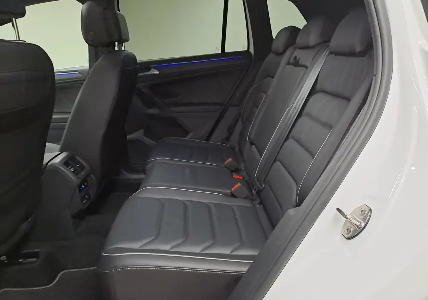 Vue intérieure côté droit des sièges arrière en cuir noir du Volkswagen Tiguan blanc nacré 2023, avec éclairage d'ambiance bleu.