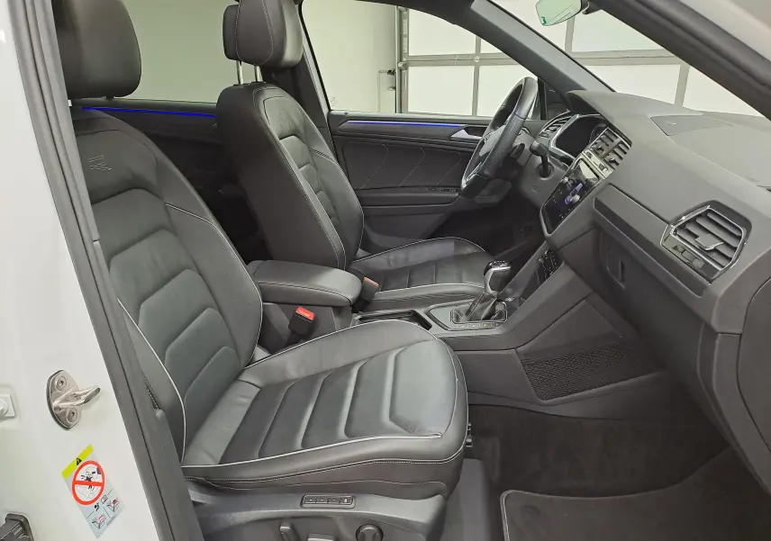 Vue intérieure côté conducteur du Volkswagen Tiguan blanc nacré 2023, sièges cuir noirs et tableau de bord moderne.