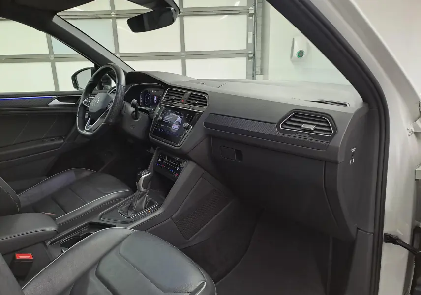 Vue intérieure côté conducteur du Volkswagen Tiguan blanc nacré 2023, avec tableau de bord et sièges en cuir noir.