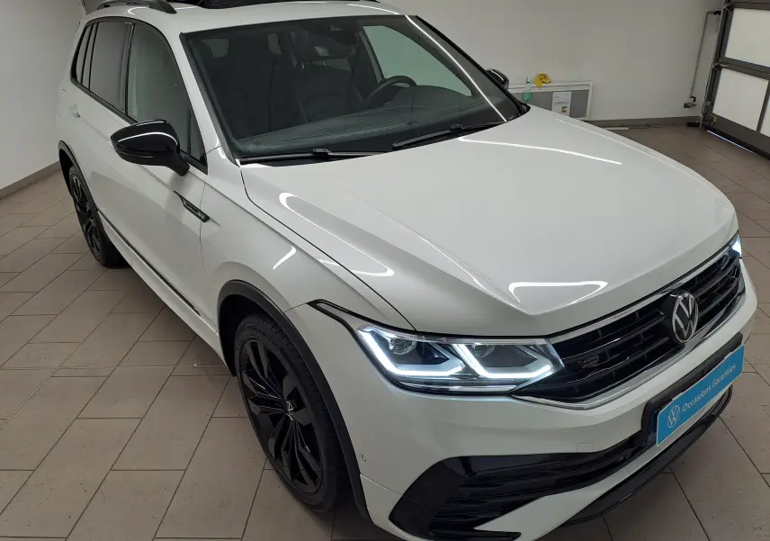 Volkswagen Tiguan blanc nacré vu en 3/4 avant droit, avec jantes noires 20'' et feux LED allumés.