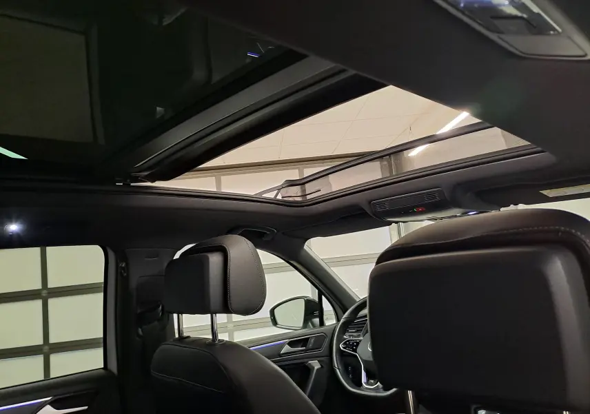 Vue intérieure du Volkswagen Tiguan 2023, toit ouvrant panoramique ouvert, sièges en cuir noir et ambiance lumineuse.
