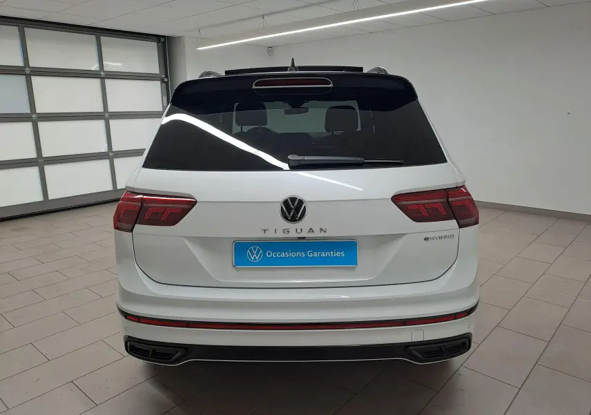 Vue arrière d'un Volkswagen Tiguan blanc nacré eHybrid 2023 avec logo et feux LED distinctifs en intérieur showroom.