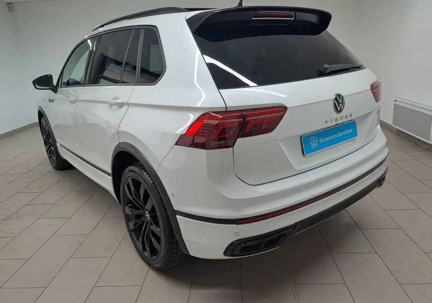 Vue 3/4 arrière droite du Volkswagen Tiguan blanc nacré avec jantes noires 20 pouces et attelage escamotable visible en intérieur.