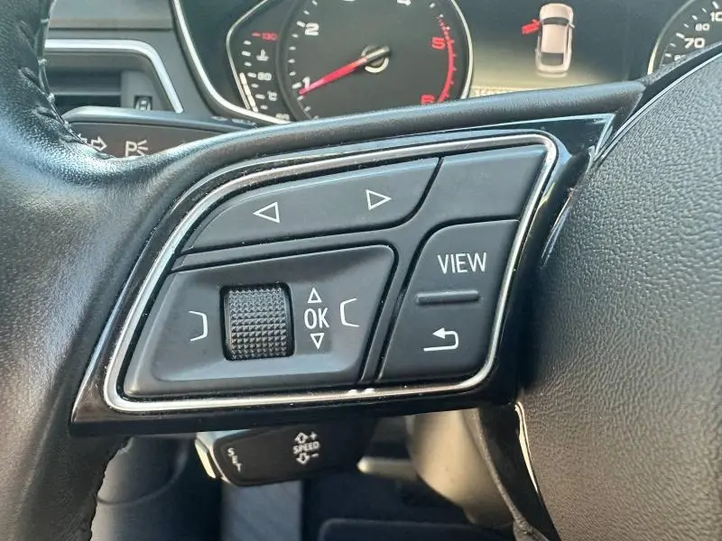 Gros plan sur les commandes multifonctions gauche du volant cuir noir de l'Audi A5 Sportback 2018, avec tableau de bord en arrière-plan.