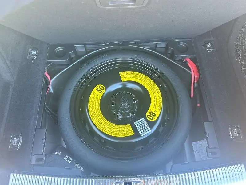 Vue plongeante sur la roue de secours compacte noire avec étiquettes jaunes dans le coffre d'une Audi A5 Sportback 2018.