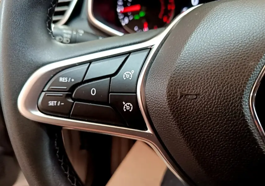 Gros plan sur les commandes du régulateur de vitesse au volant cuir noir de la Renault Clio Business blanche de 2021.