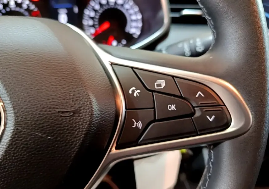 Gros plan sur les commandes multifonctions noires et argentées du volant cuir de la Renault Clio Business blanche, avec tableau de bord flou en arrière-plan.