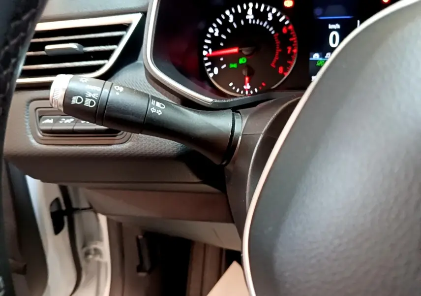 Gros plan sur le commodo des phares et clignotants à gauche du volant noir dans l’habitacle d’une Renault Clio blanche.
