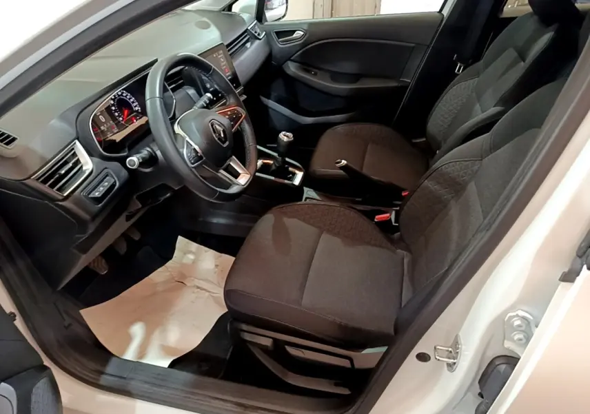 Vue intérieure côté conducteur de la Renault Clio Business blanche, montrant les sièges noirs et le volant multifonctions.
