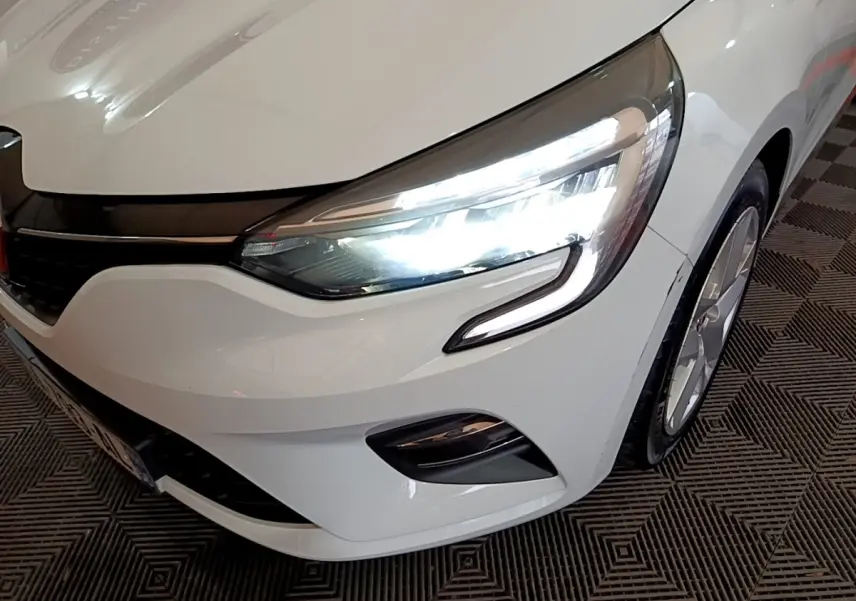 Gros plan sur l'avant droit d'une Renault Clio blanche 2021 avec phares LED allumés et jante visible.