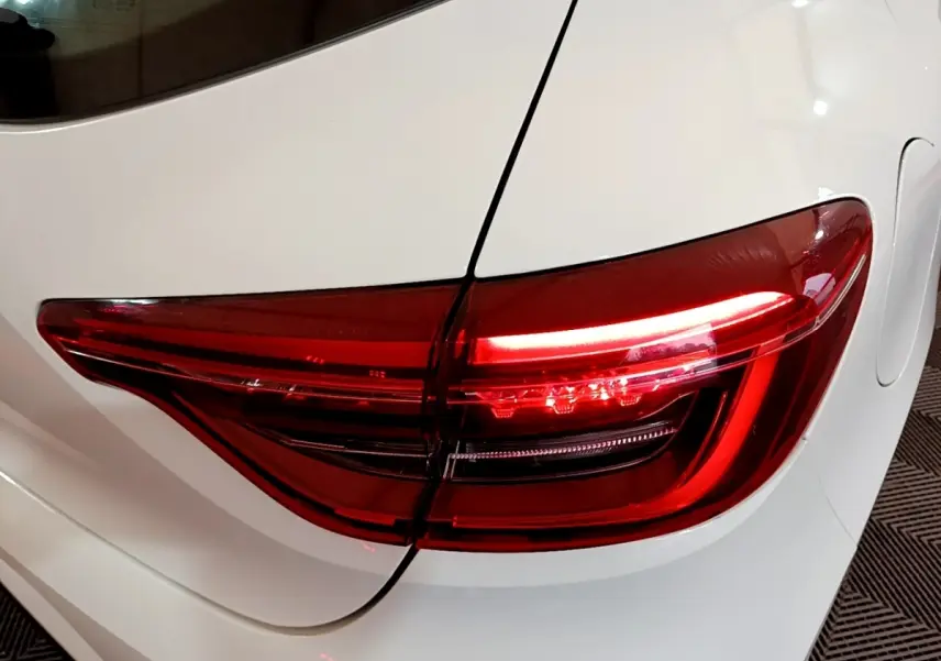Feu arrière droit allumé sur Renault Clio Business blanche, vue rapprochée du coffre et de la portière arrière.