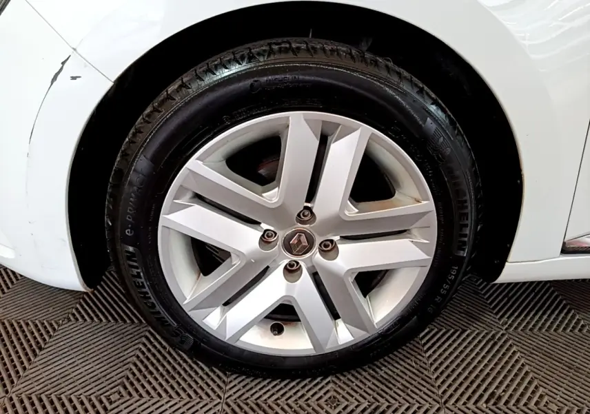 Gros plan sur la roue avant droite d'une Renault Clio blanche, jante alliage argentée au design moderne.