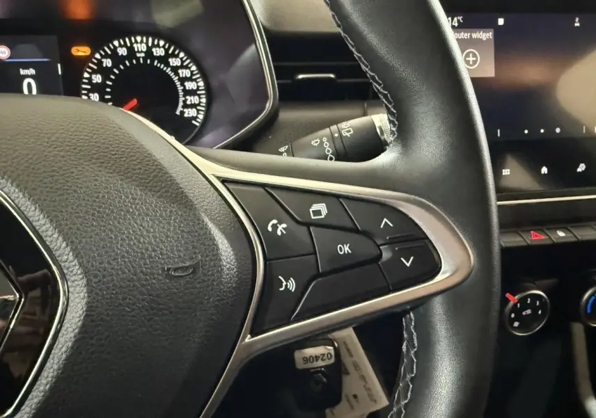 Gros plan sur le volant multifonction en cuir noir de la Renault Clio Business, avec tableau de bord et écran tactile en arrière-plan.