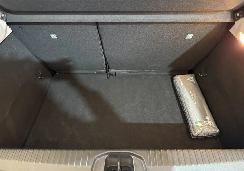 Coffre ouvert vu de dessus d'une Renault Clio Business blanche, avec un kit de sécurité gris posé à droite.