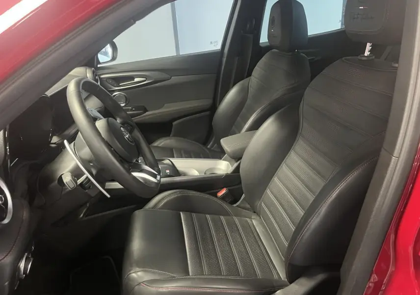 Vue intérieure côté conducteur de l'Alfa Romeo Tonale rouge 2024 avec sellerie cuir noir et surpiqûres rouges.