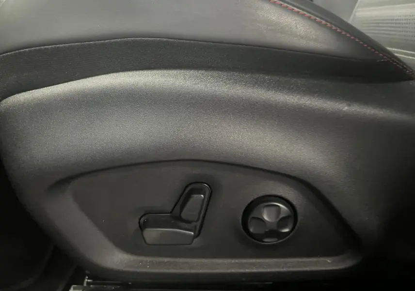 Gros plan sur les commandes électriques de réglage du siège en cuir noir avec surpiqûres rouges de l'Alfa Romeo Tonale rouge.