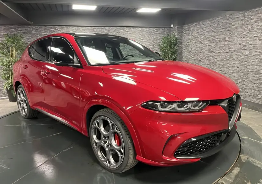 Vue 3/4 avant gauche de l'Alfa Romeo Tonale rouge avec jantes 20 pouces et toit noir en intérieur showroom.