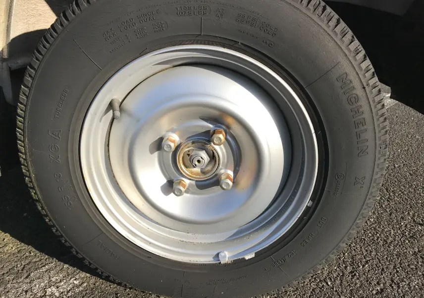 Gros plan sur la roue avant droite du Citroën C15 Isotherm blanc de 1997 avec jante acier et pneu Michelin.