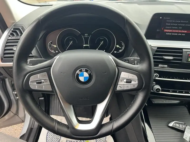 Vue intérieure centrée sur le volant cuir multifonction d'une BMW X3 xDrive30eA 2020, avec tableau de bord et écran tactile visibles.