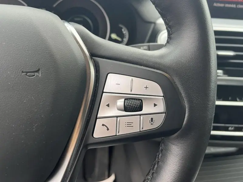 Gros plan sur les commandes multifonctions en aluminium brossé du volant cuir noir d'une BMW X3 xDrive30eA 2020.