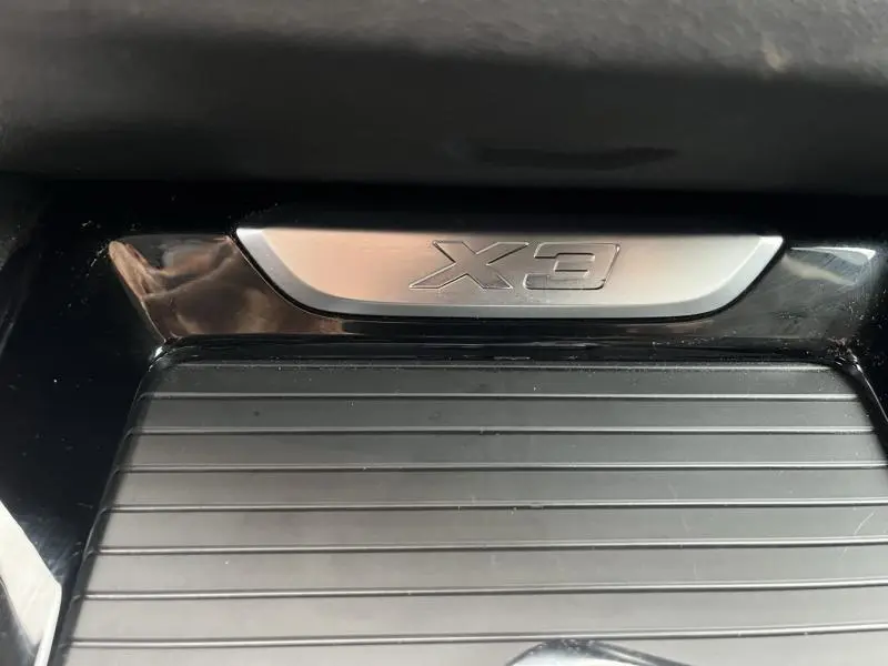 Gros plan sur la plaque intérieure X3 en métal brossé avec surface noire striée, intérieur BMW xDrive30eA 2020.