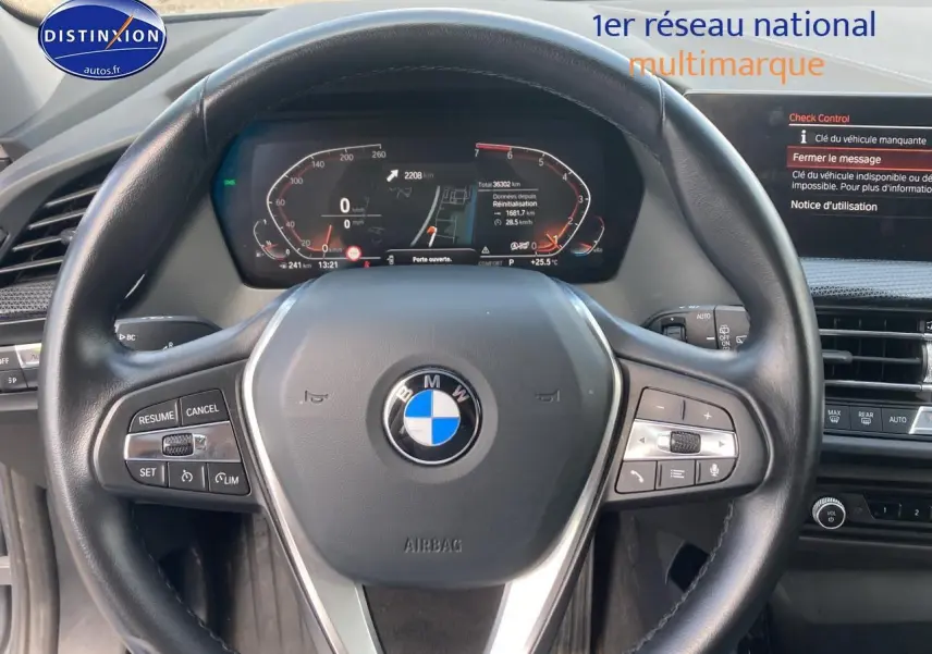 Vue rapprochée du volant cuir noir multifonction de la BMW Série 1 118i 2023 avec tableau de bord digital allumé.