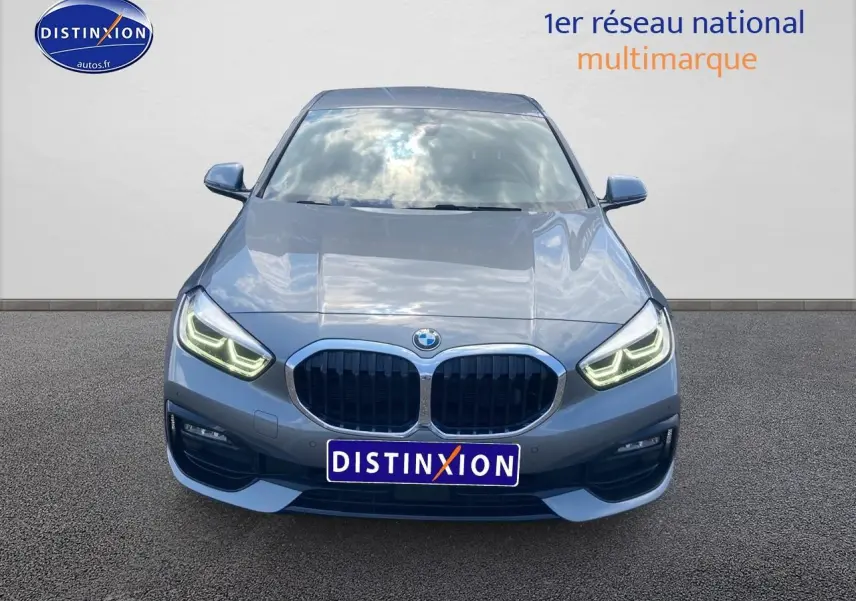 Vue frontale d'une BMW Série 1 gris foncé 2023 avec phares LED allumés et calandre caractéristique double haricot.