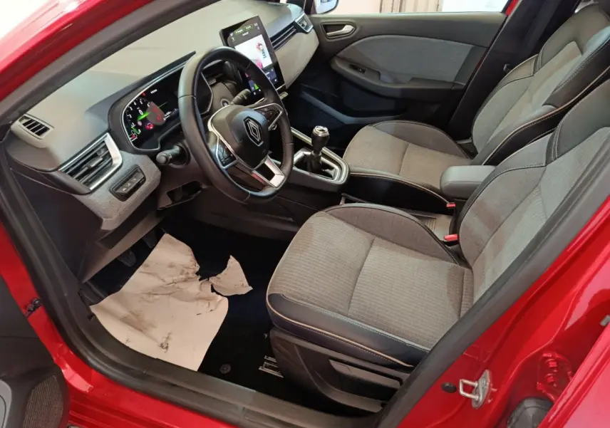 Vue intérieure côté conducteur de la Renault Clio Techno TCe 90 rouge 2024 avec tableau de bord numérique et sièges tissu gris.
