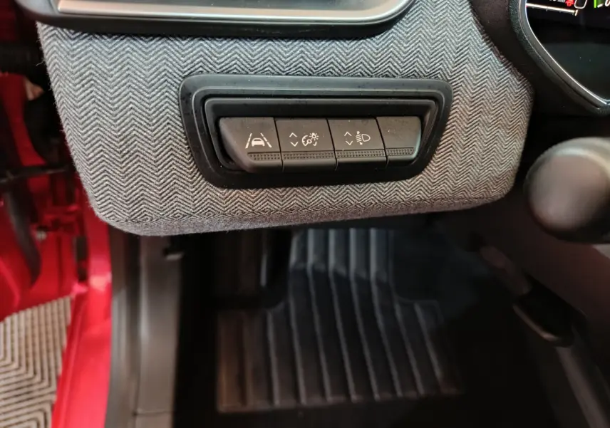 Détail des commandes d'assistance à la conduite sur tableau de bord gris, intérieur rouge visible côté conducteur Renault Clio 2024.