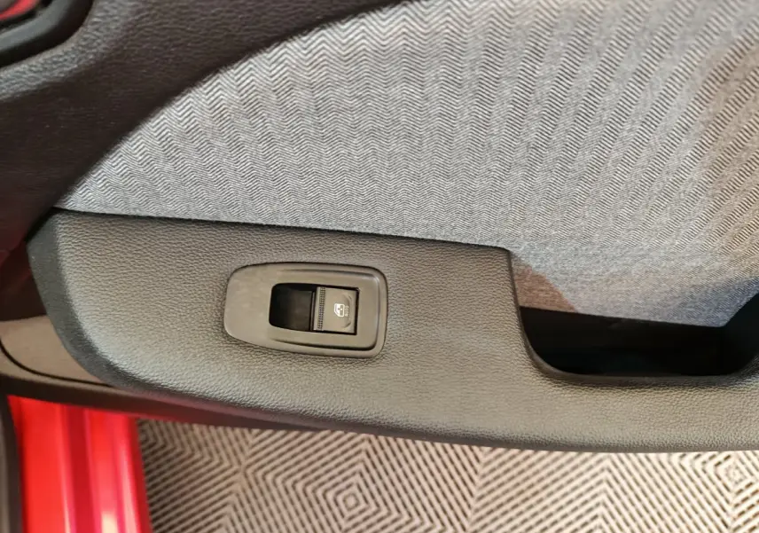 Gros plan sur le bouton de commande de la vitre arrière dans la portière côté gauche d’une Renault Clio Techno TCe 90 rouge.