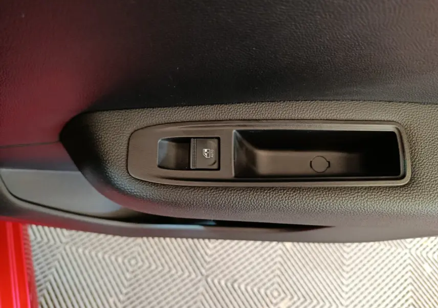 Gros plan sur le bouton de commande de la vitre électrique côté conducteur dans une Renault Clio rouge 2024.